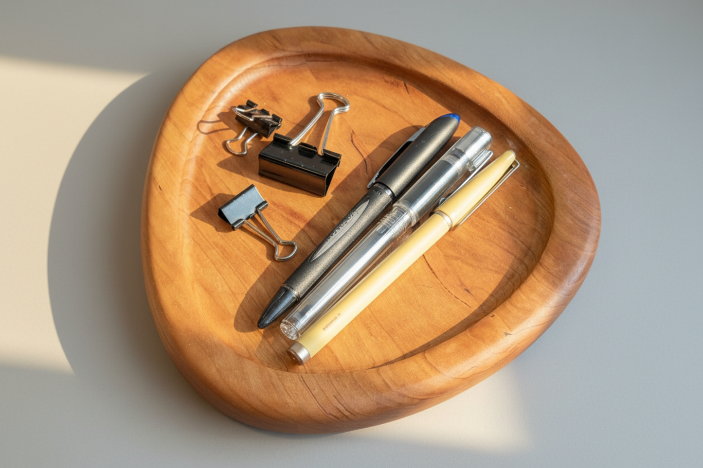 Wooden tray with office supplies including pens and clips on a neutral background