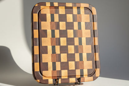 Wooden cutting board with a checkered pattern on a light wooden surface.